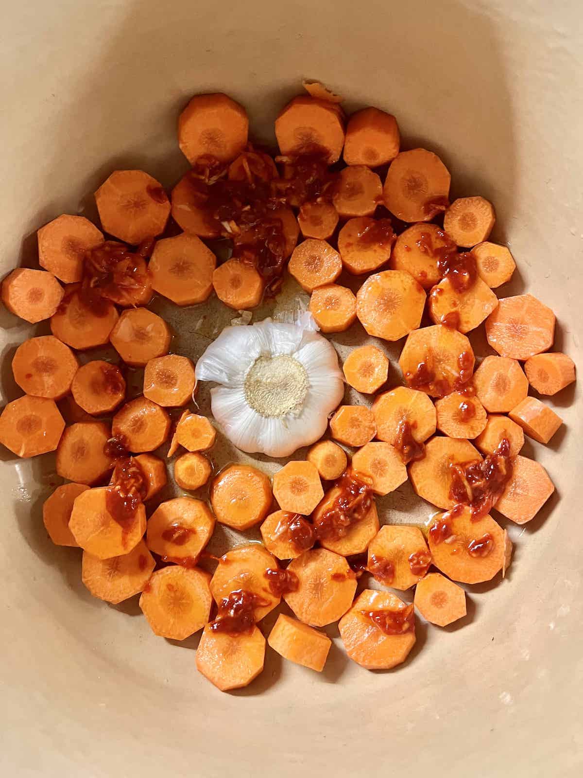 Chopped carrots around a garlic bulb in a Dutch oven.