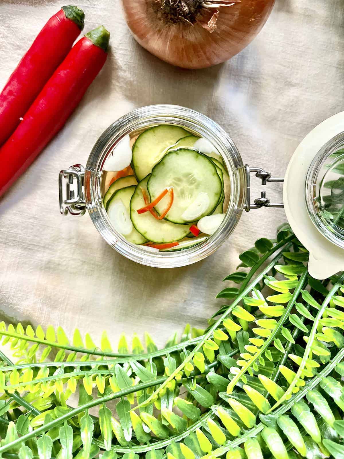 Overhead shot of thinly sliced cucumbers and red chillies in a glass jar.