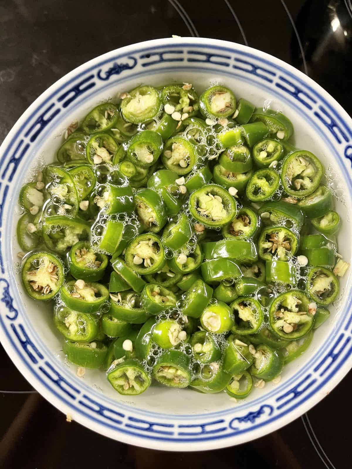 Sliced green chilies soaking in a bowl of hot water.
