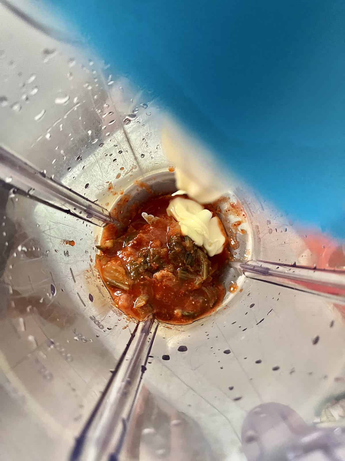 Overhead shot of mayonnaise being added to kimchi in a blender.