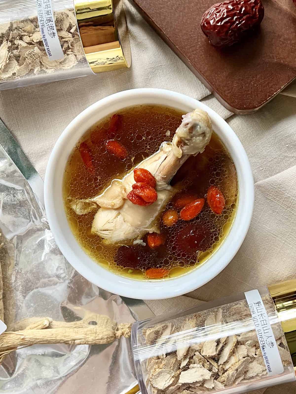 A bowl of a chicken drumstick and goji berries in soup.