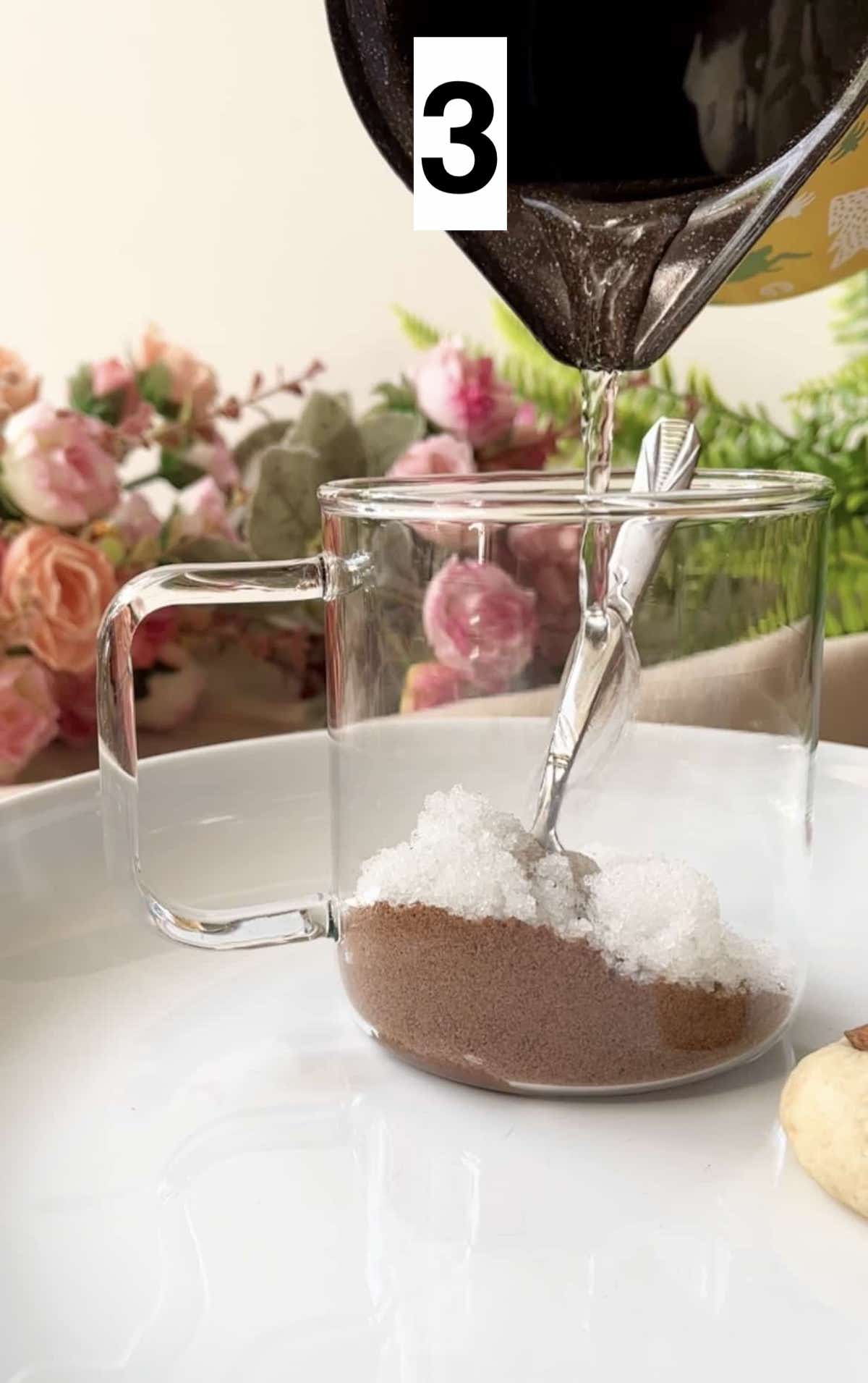 Pouring hot water into a glass cup of milo powder and sugar.