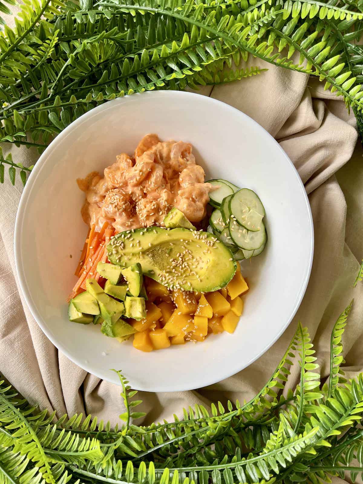 A bowl of rainbow poke rice with avocado, spicy shrimp, mango and cucumber.