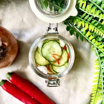 A jar of homemade pickled cucumbers with chilies and an onion next to it.