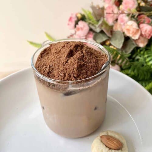 A glass of dinosaur milo with an almond cookie on the side.