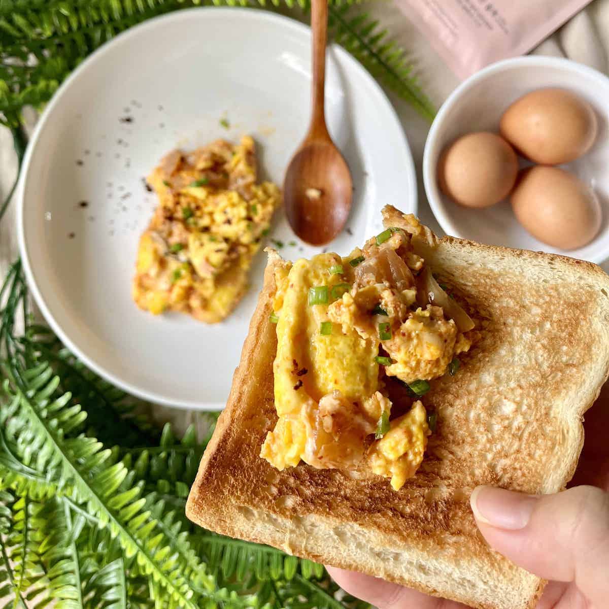 A half bitten piece of toast with kimchi and scrambled eggs on it.