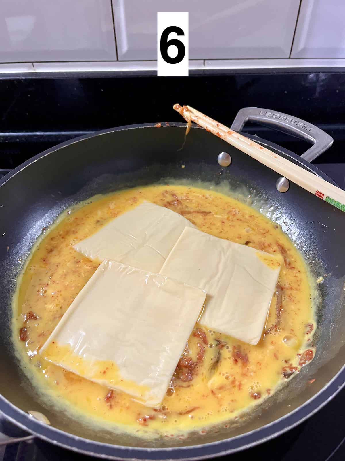 Cheese on top of beaten egg and kimchi in a pan.