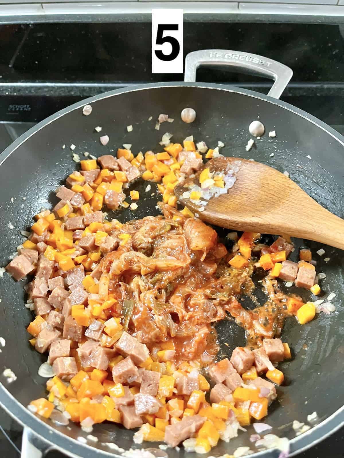 Stir-frying kimchi with spam, carrots, onions and garlic.