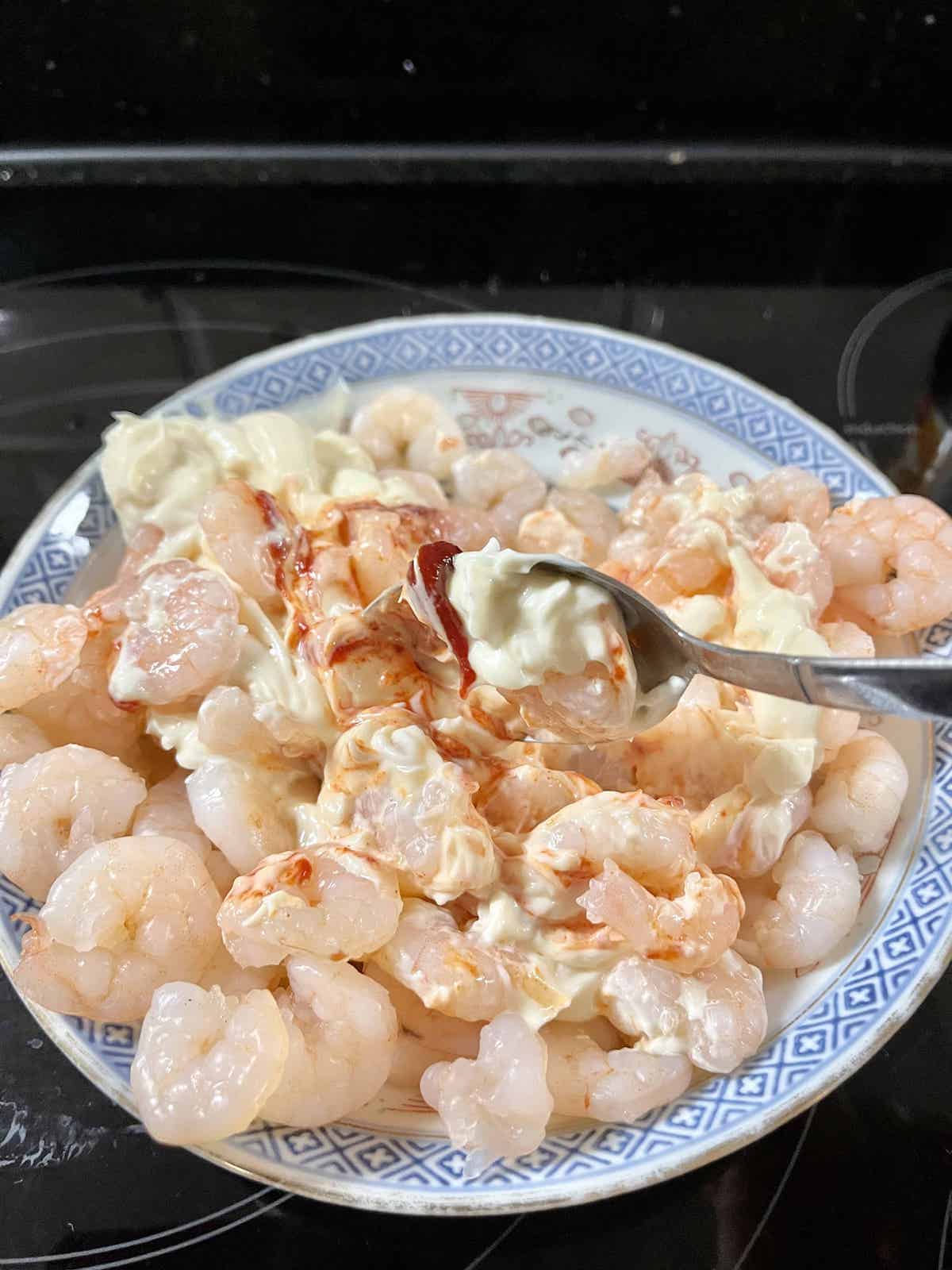 Mixing poached shrimp with sambal and sriracha chili sauce.