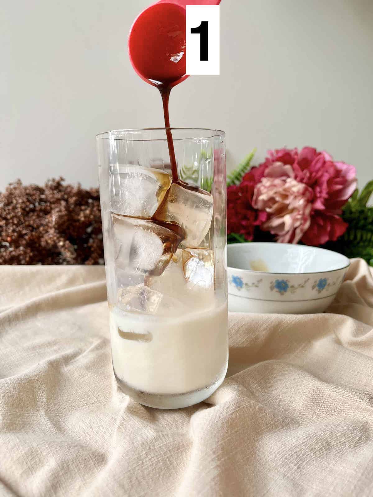 Adding maple syrup to a glass of ice and milk.