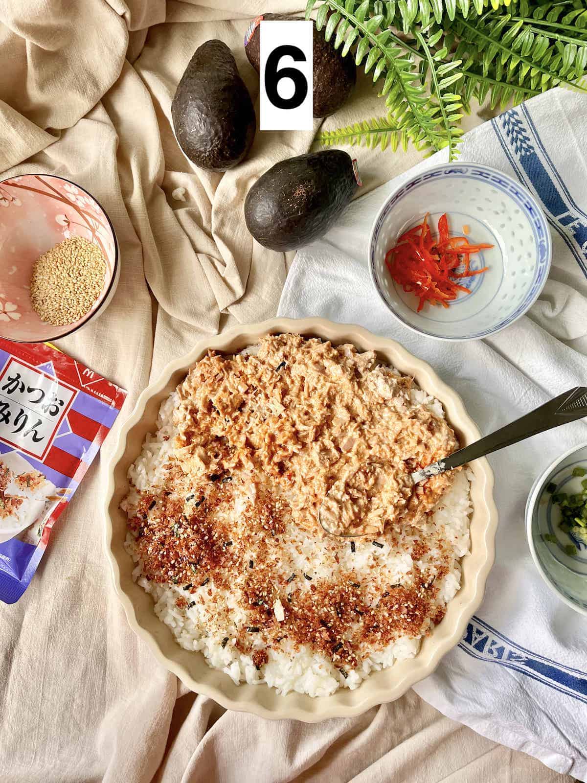 Applying tuna, cream cheese and mayo spread to the top of sushi rice.