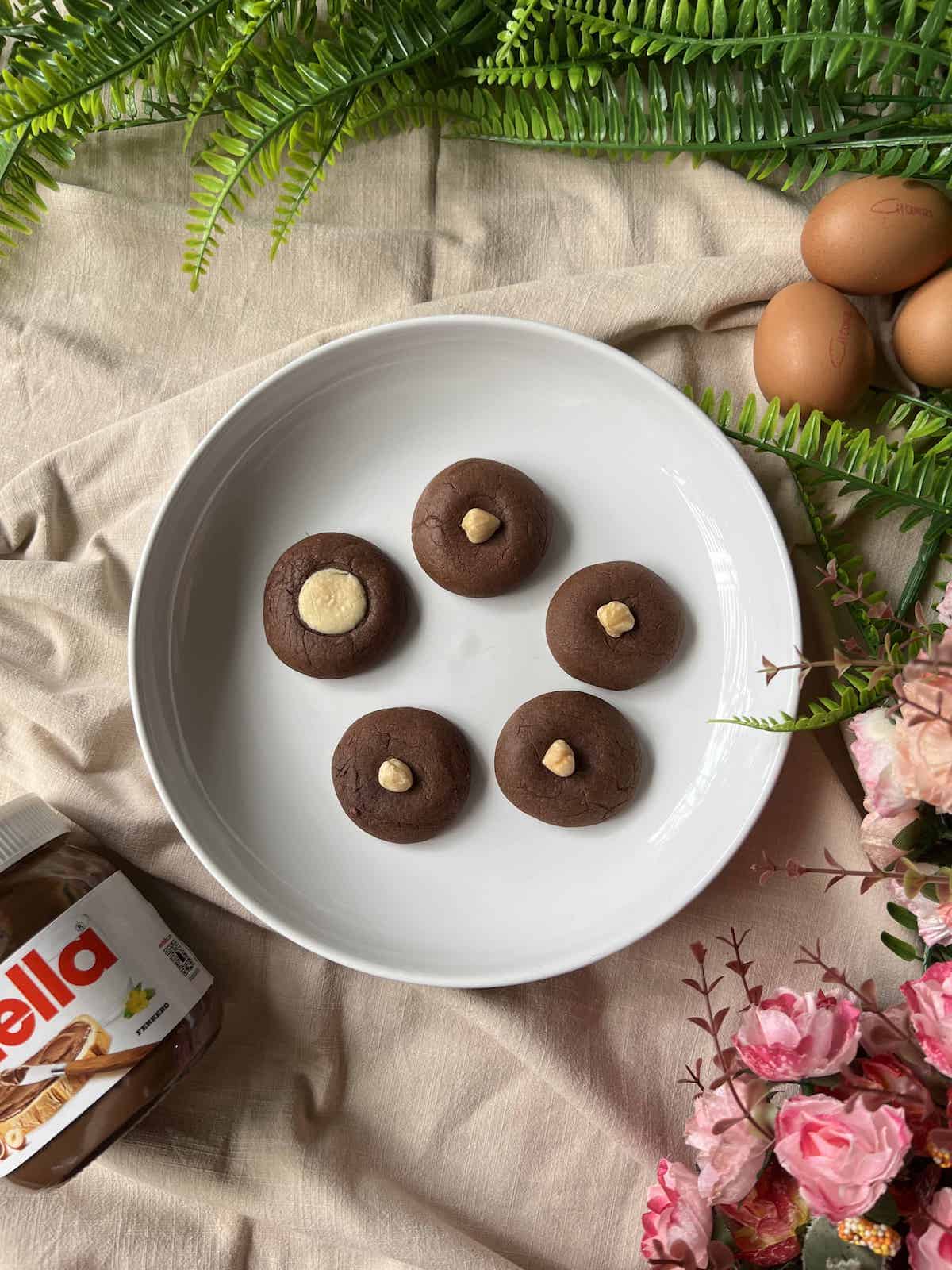 A plate with 5 Nutella cookies, 1 with a chocolate centre, the rest with hazelnuts.