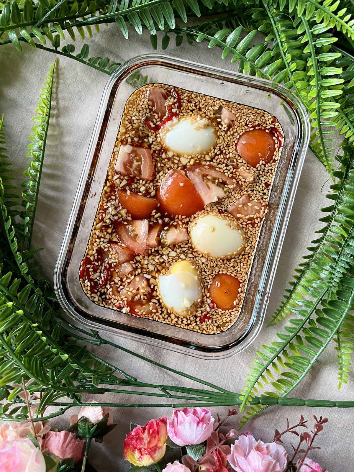 Marinating soft boiled eggs sesame seeds, tomatoes and onions in a soy sauce mixture.