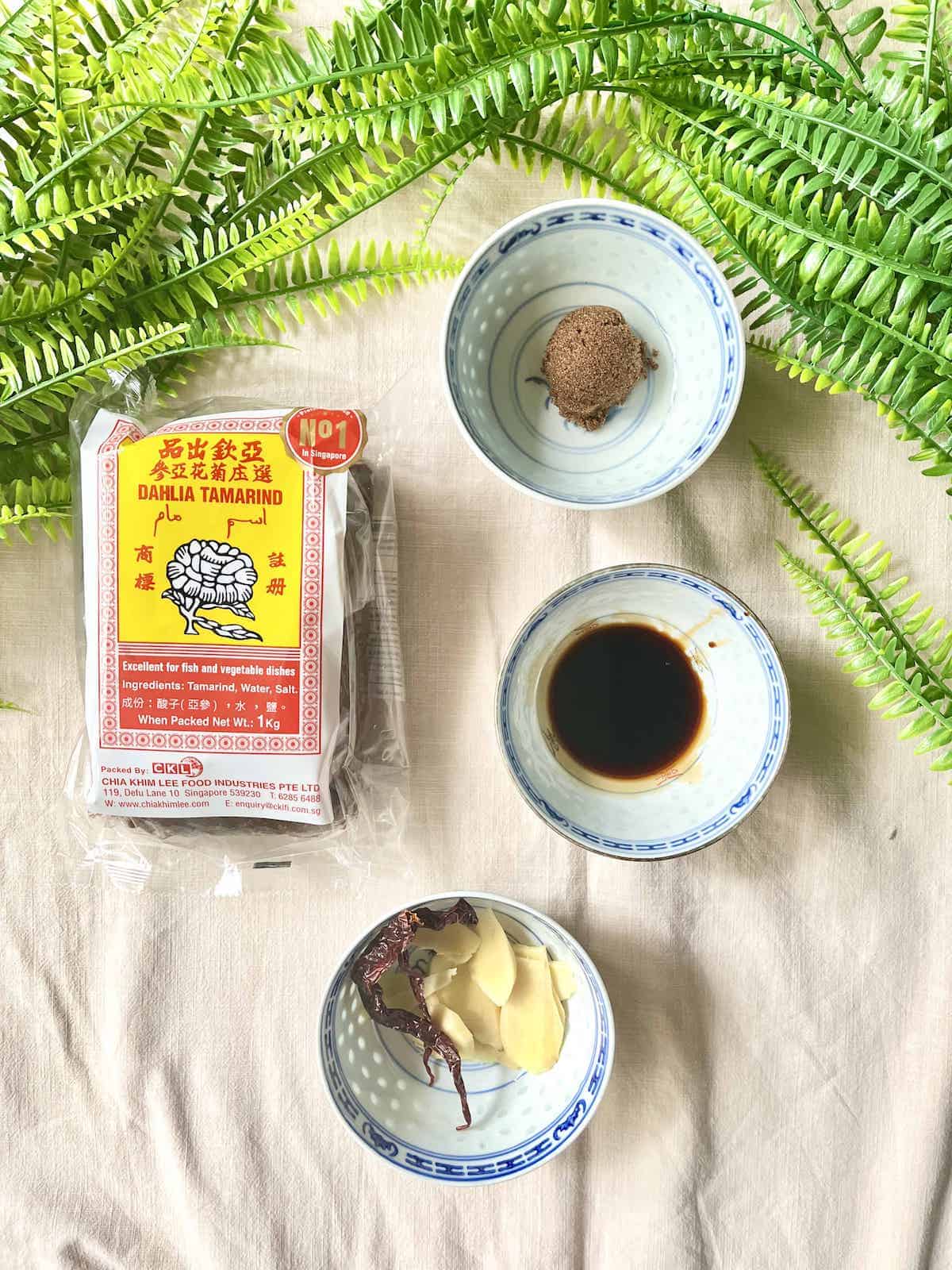 A packet of tamarind, brown sugar, soy sauce, ginger and chilies next to each other.