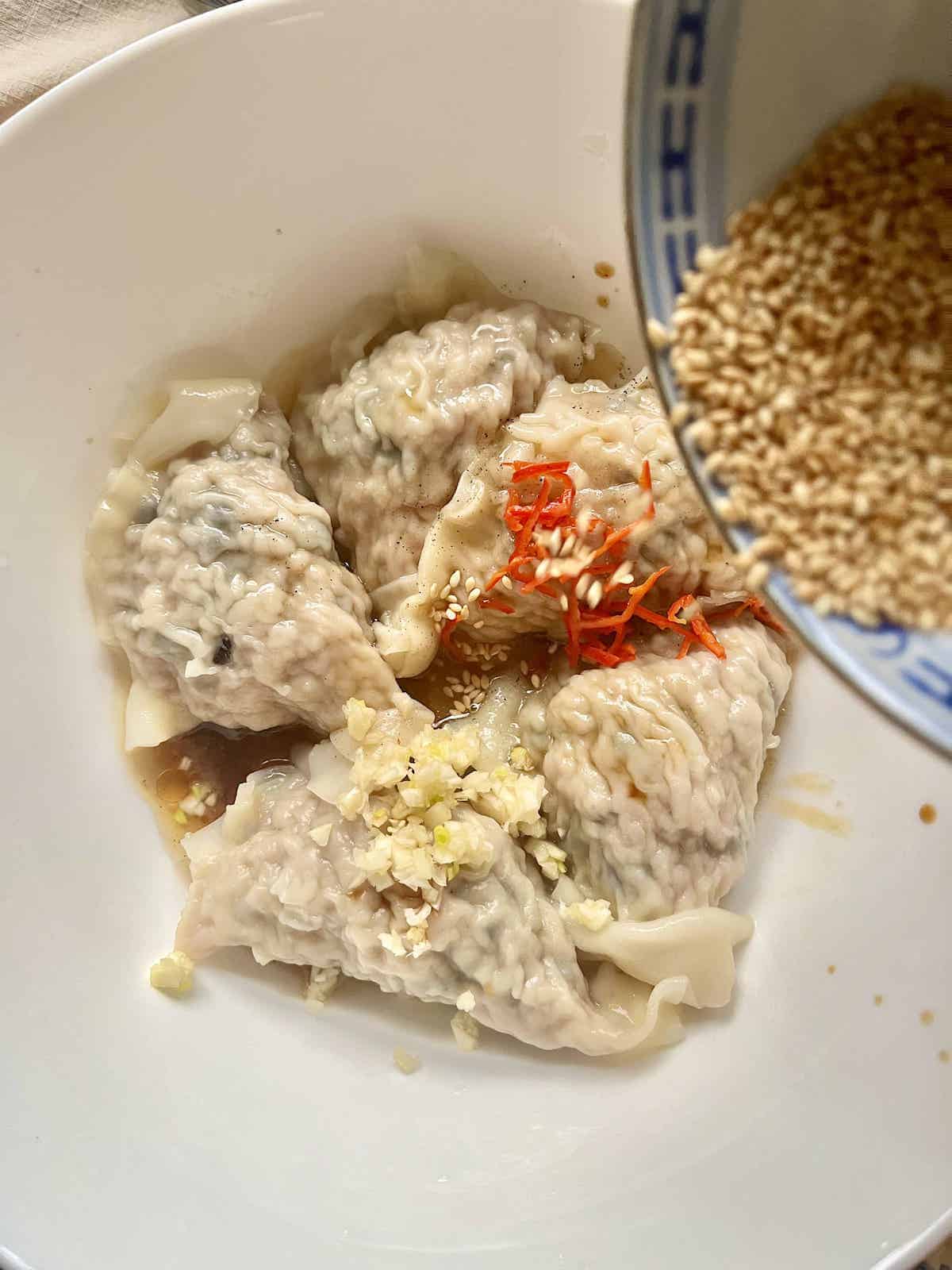 Pouring sesame seeds onto garlic, soy sauce, chili and dumplings.