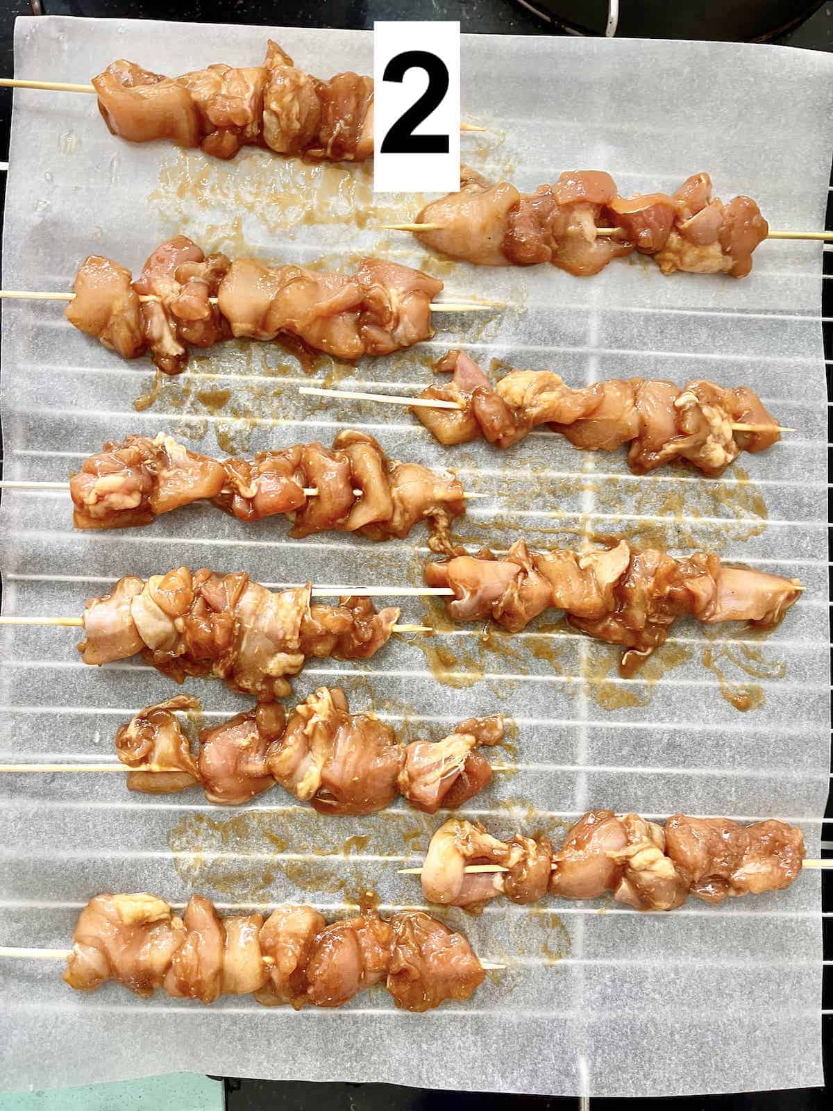 Chicken chunks on bamboo skewers laid out on a baking tray.