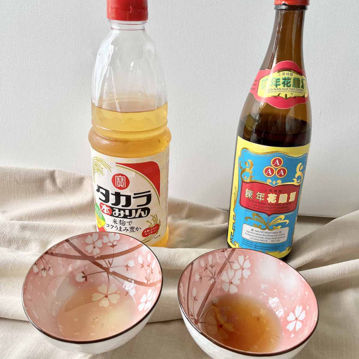 A bottle of hon-mirin next to a bottle of shaoxing, with some of each in bowls.