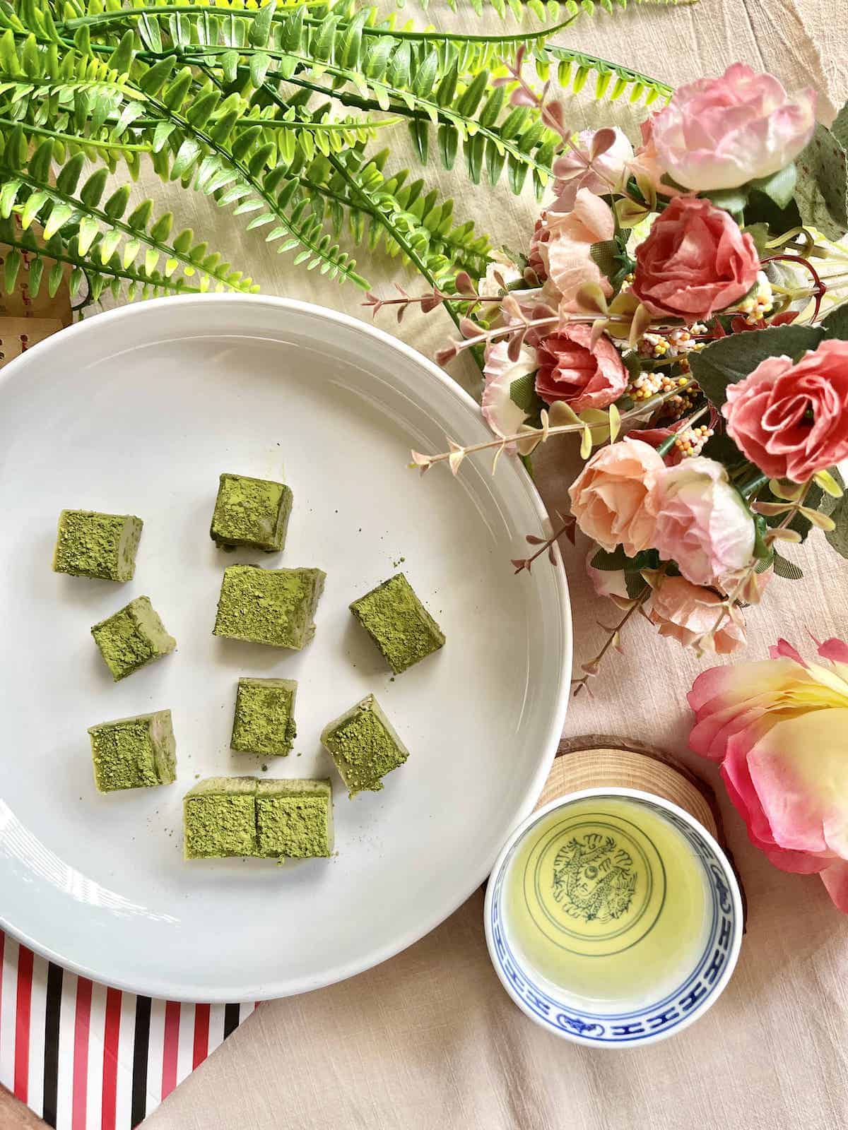 Pieces of homemade matcha chocolate next to a cup of green tea.