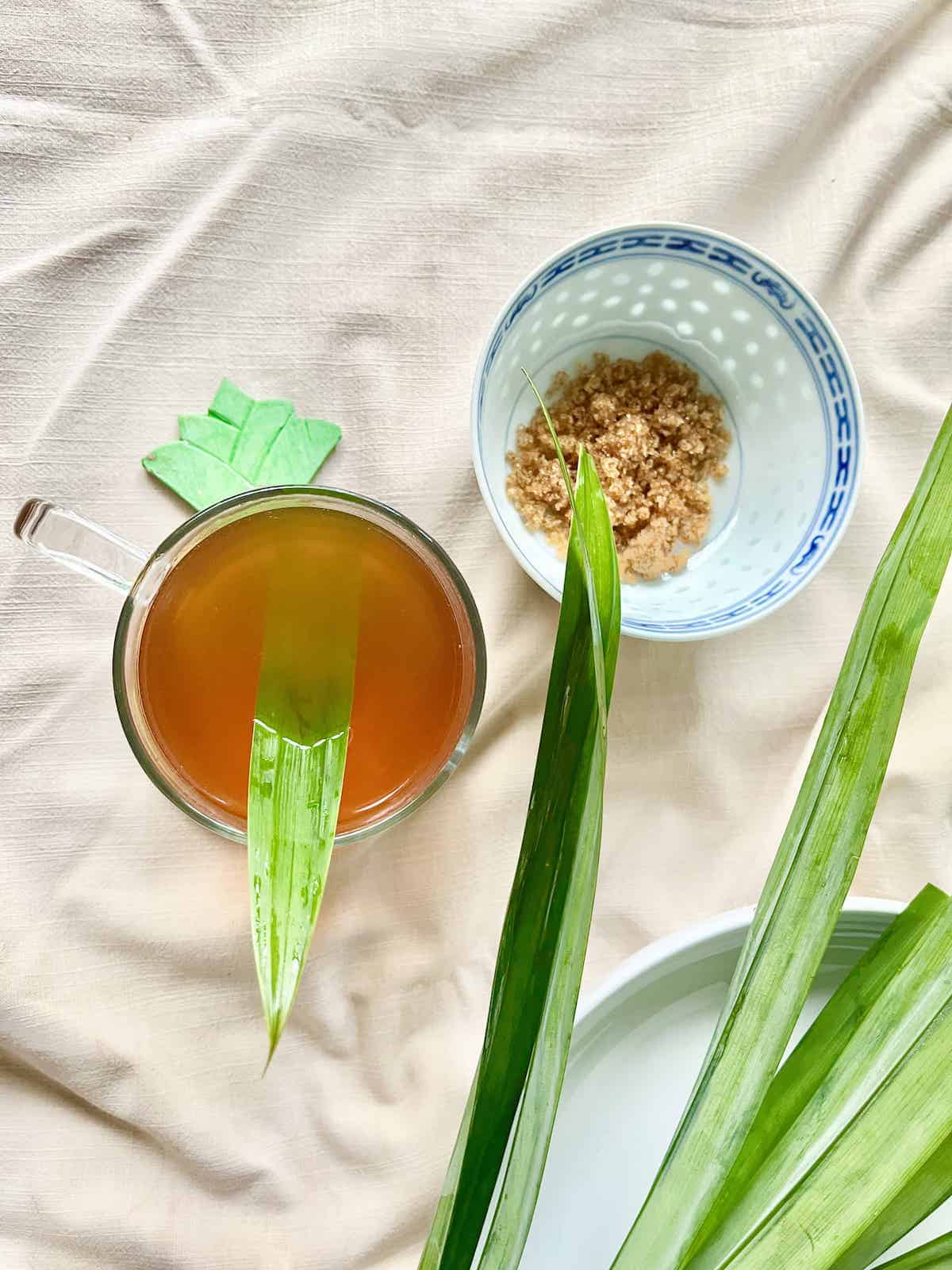 Overhead shot of a cup of pandan tea next to brown sugar.