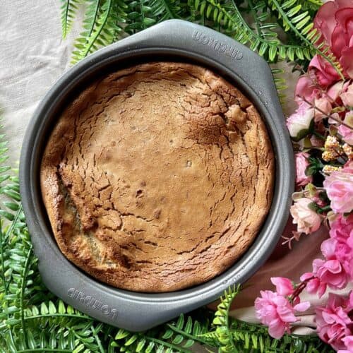 Baked Nian Gao in a round cake tin next to Chinese New Year flowers.