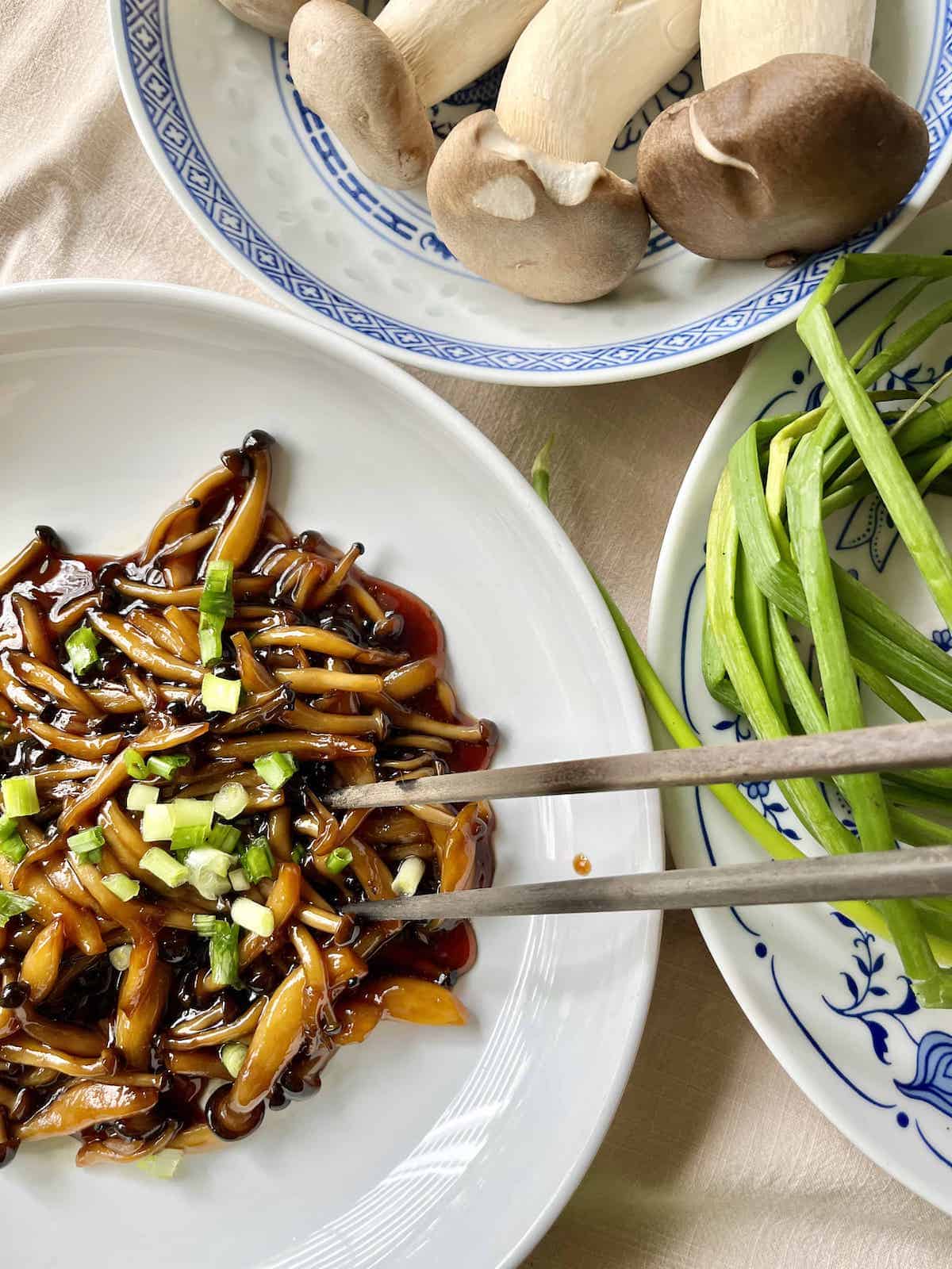 Using chopsticks to pick up teriyaki shimeji mushrooms from a white plate.