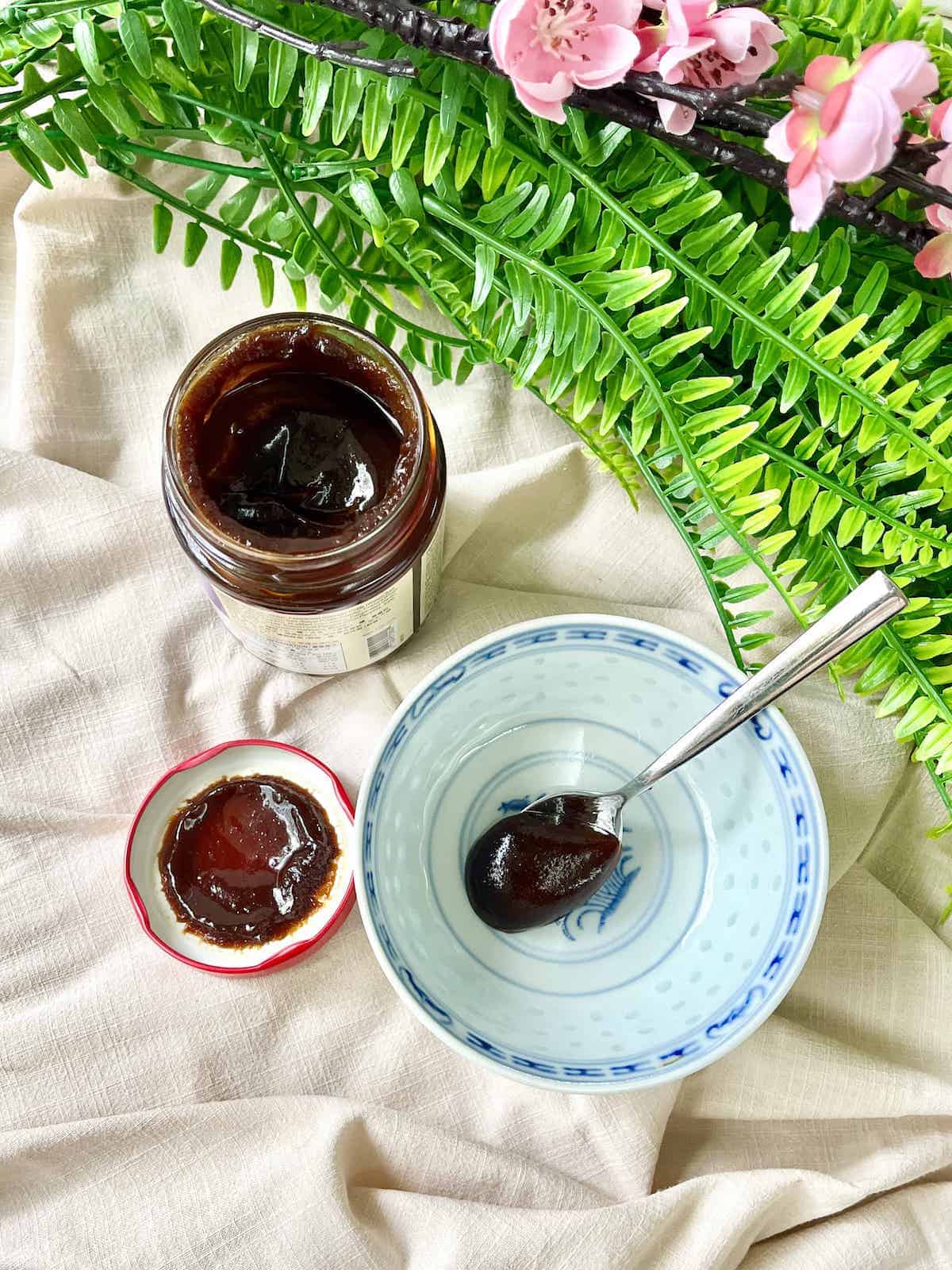 A teaspoon of hoisin sauce next to an open Lee Kum Kee jar.
