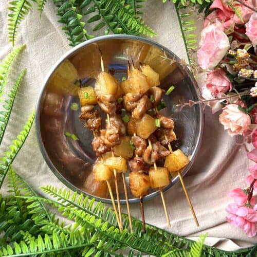 Several pineapple teriyaki chicken skewers on a silver plate.