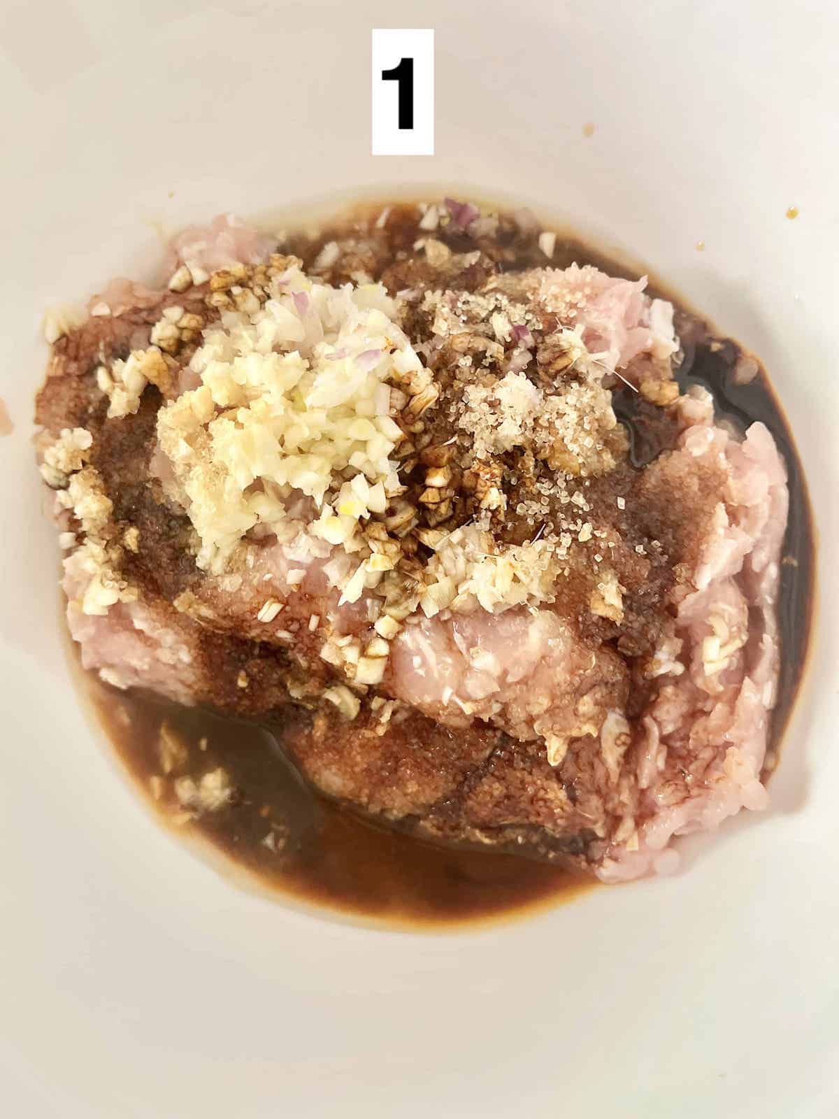 Ground chicken marinating with minced lemongrass, minced garlic, minced shallots, and sauces in a white bowl.