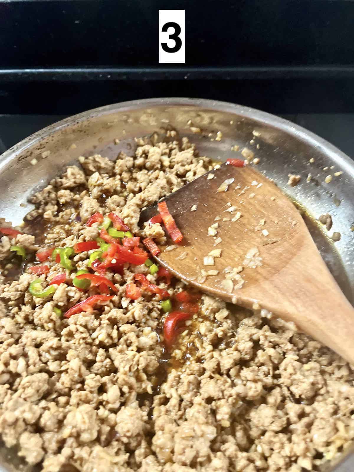 Sliced chilies on cooked minced chicken in a silver pan.