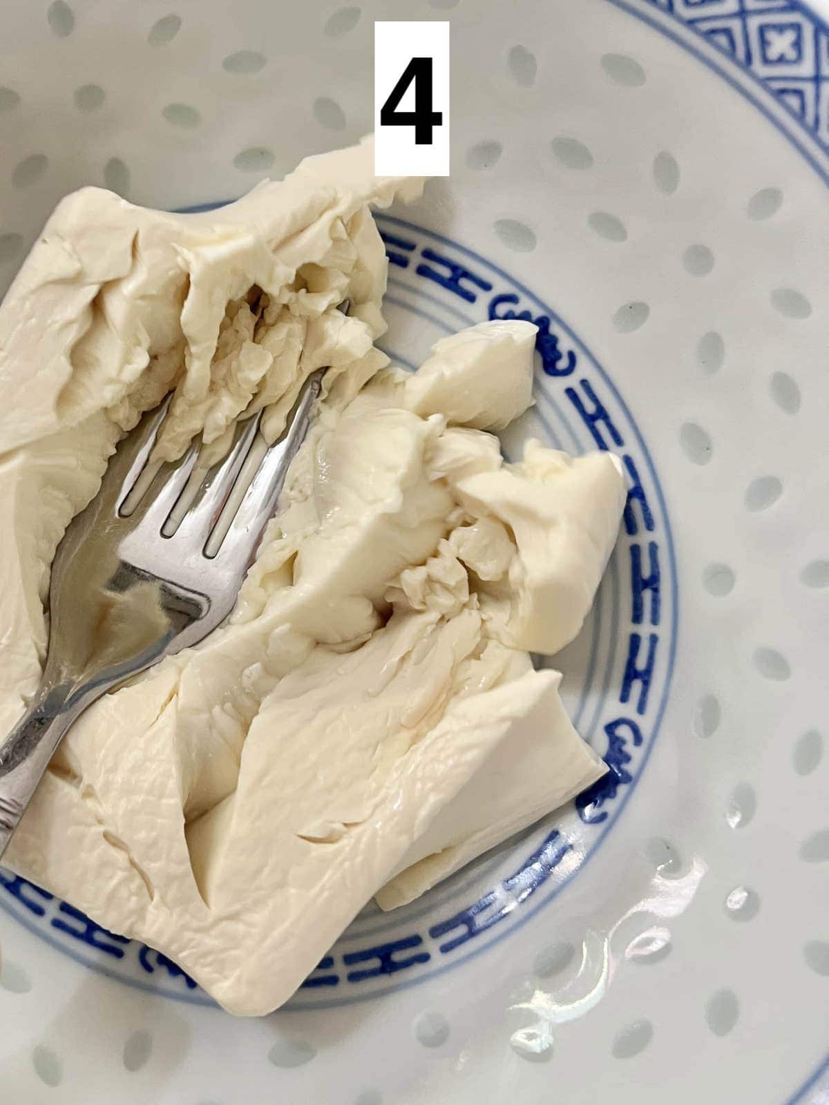 Mashing up a block of tofu with a fork.
