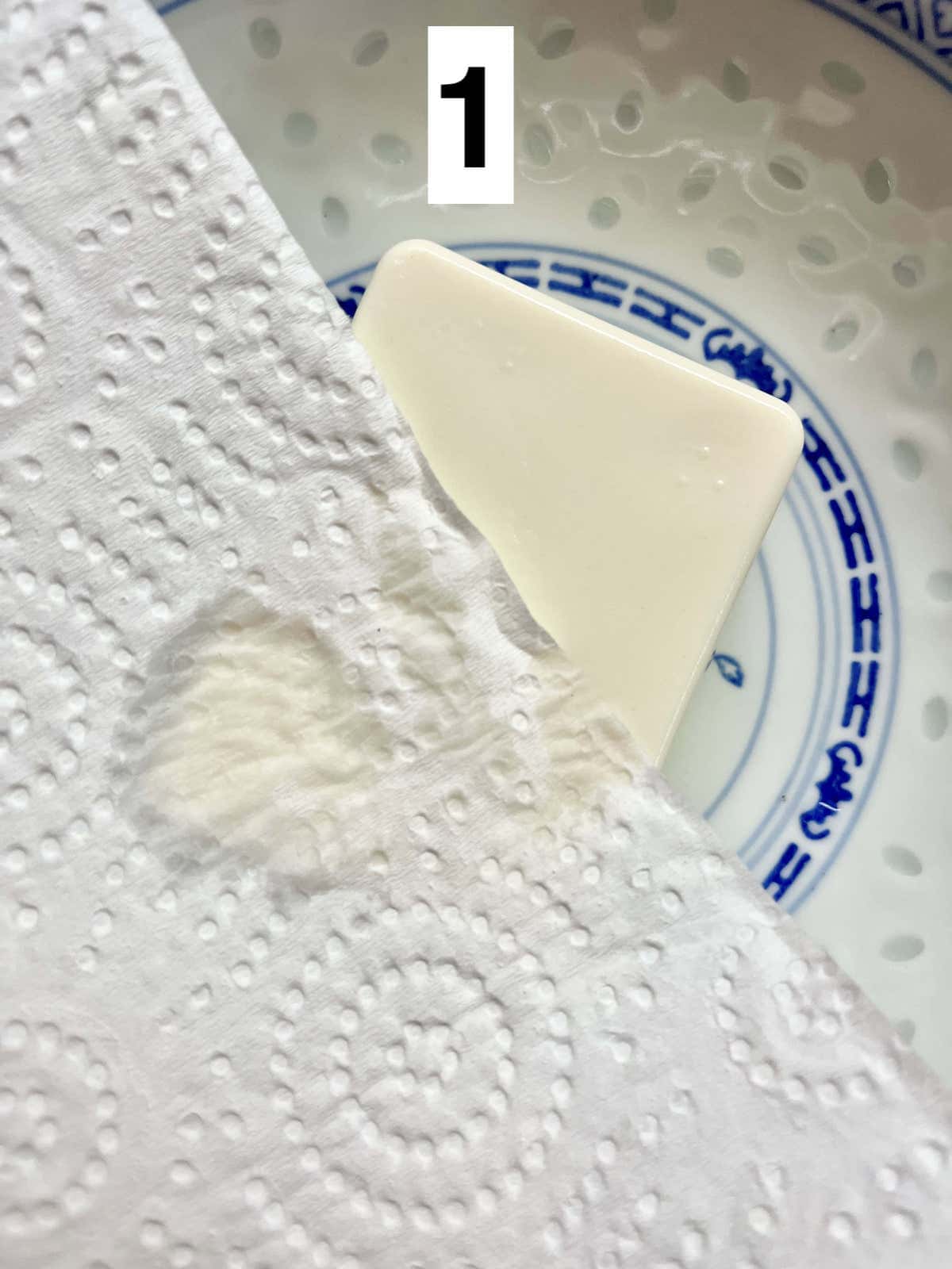 Patting a block of tofu with a kitchen towel.