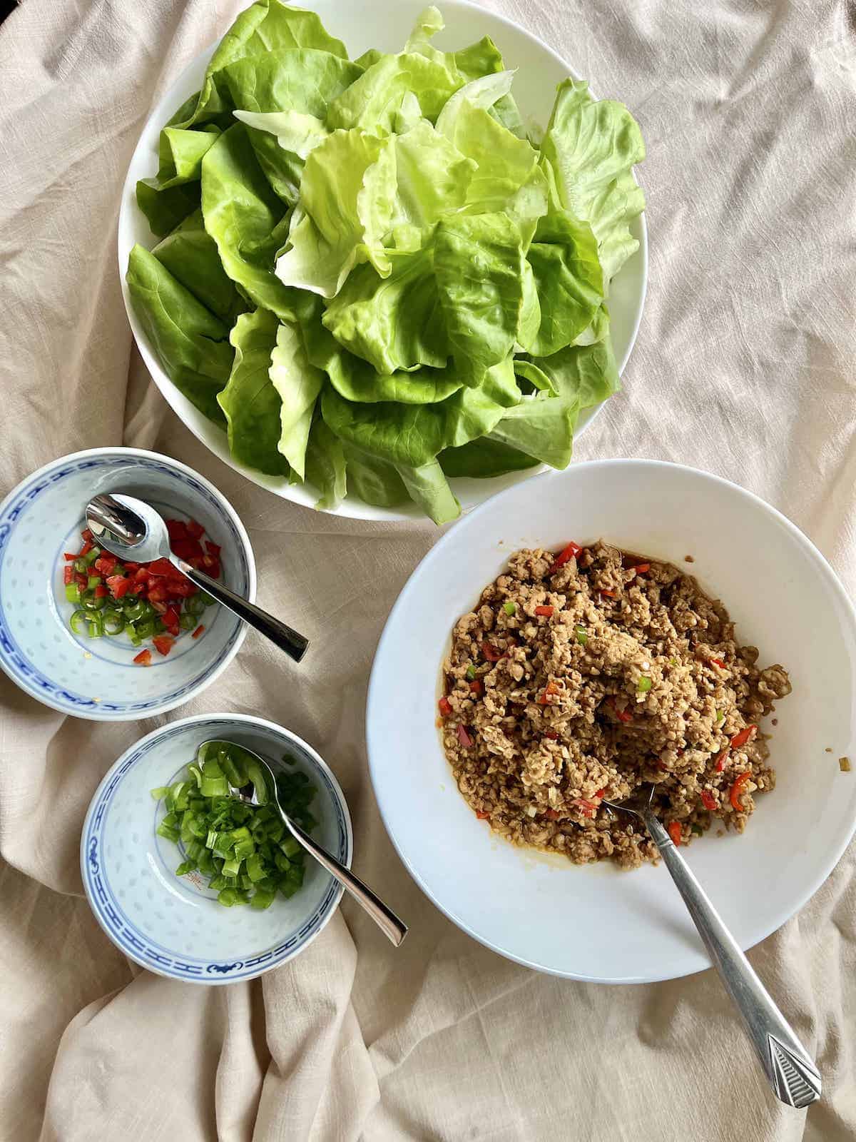 A bowl of ground chicken next to lettuce leaves, sliced chilies and spring onions.