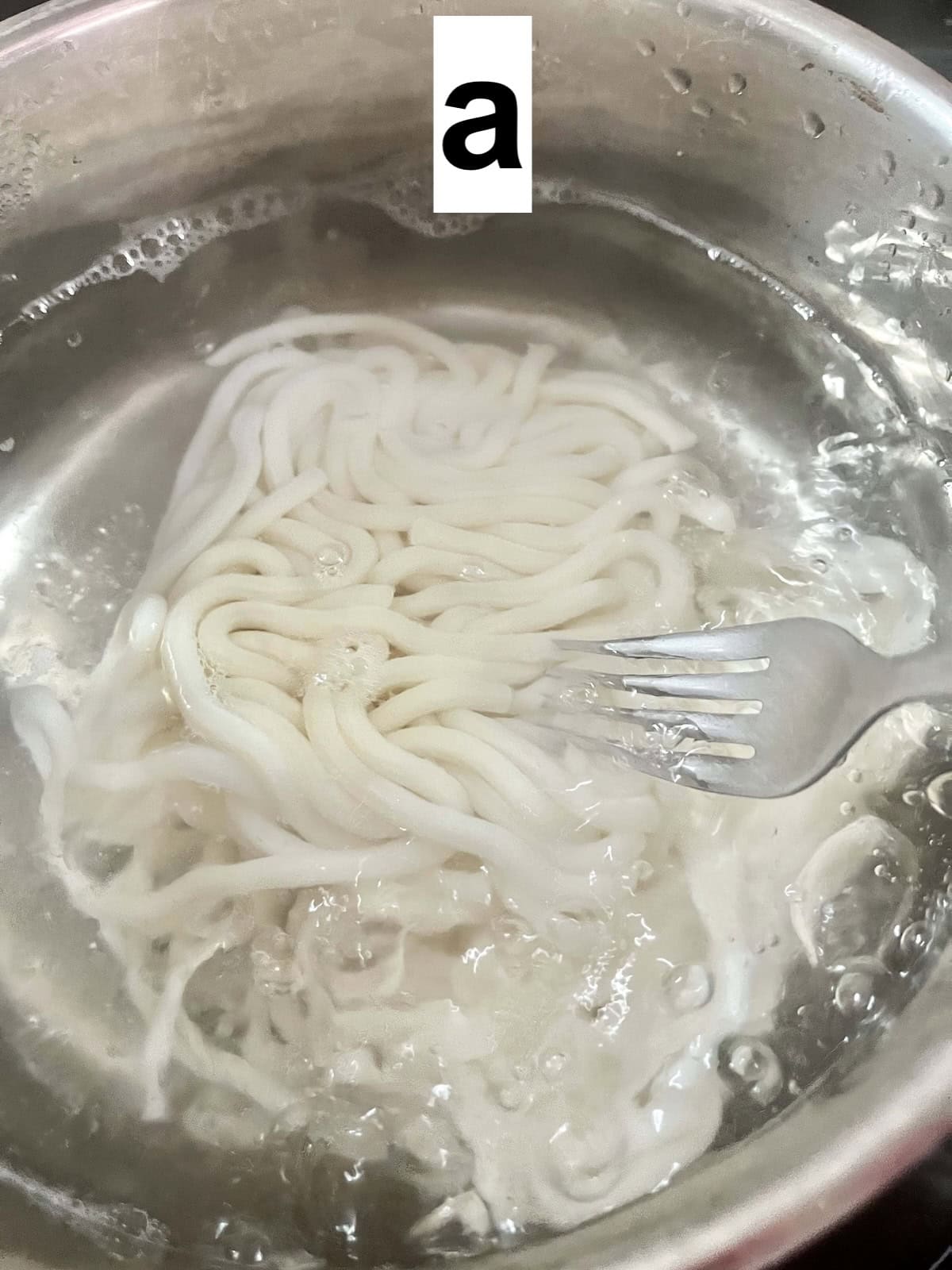 Using a fork to separate udon noodles in a pot of boiling water.