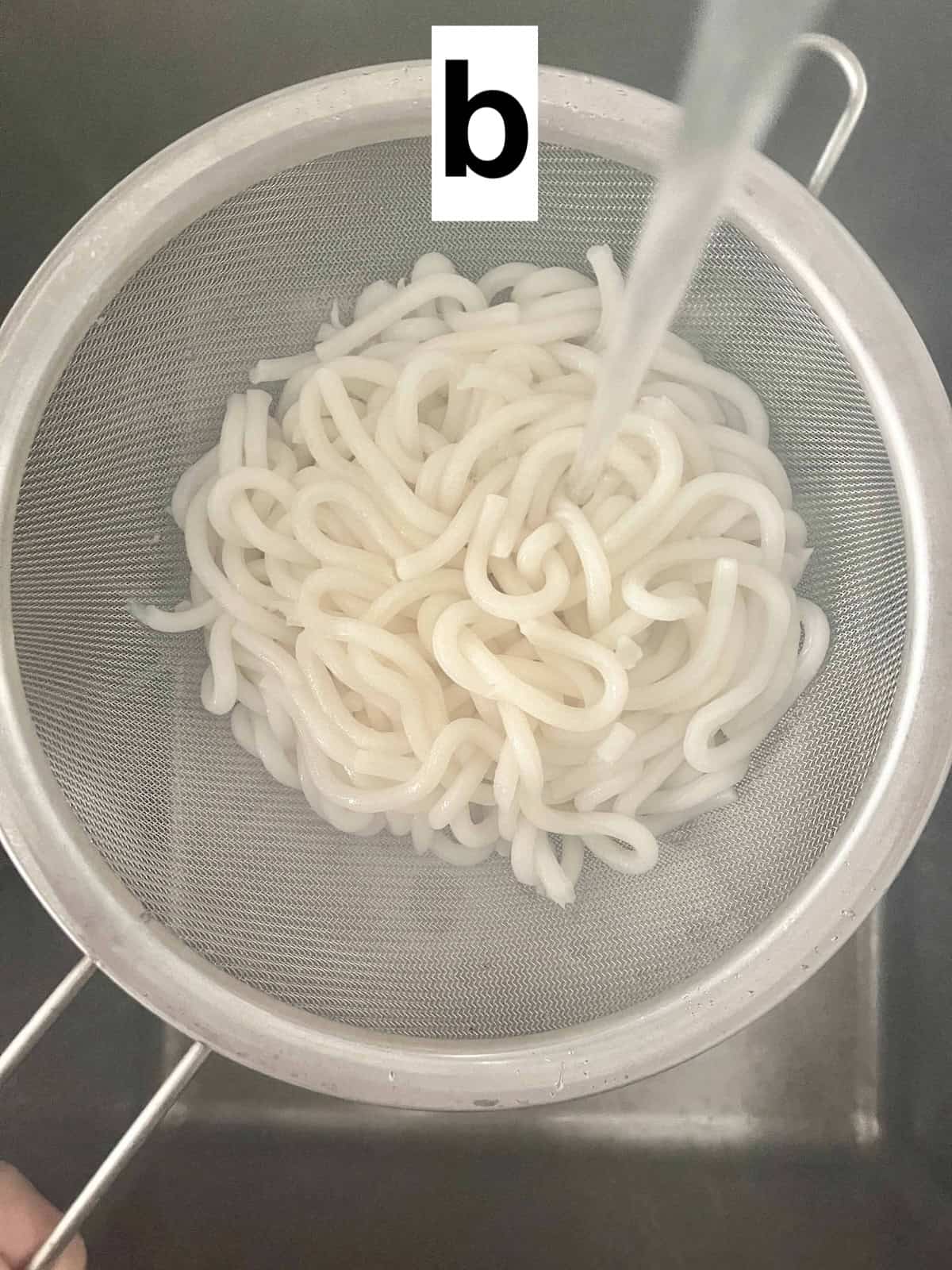 Rinsing cooked udon noodles under the tap in a colander.