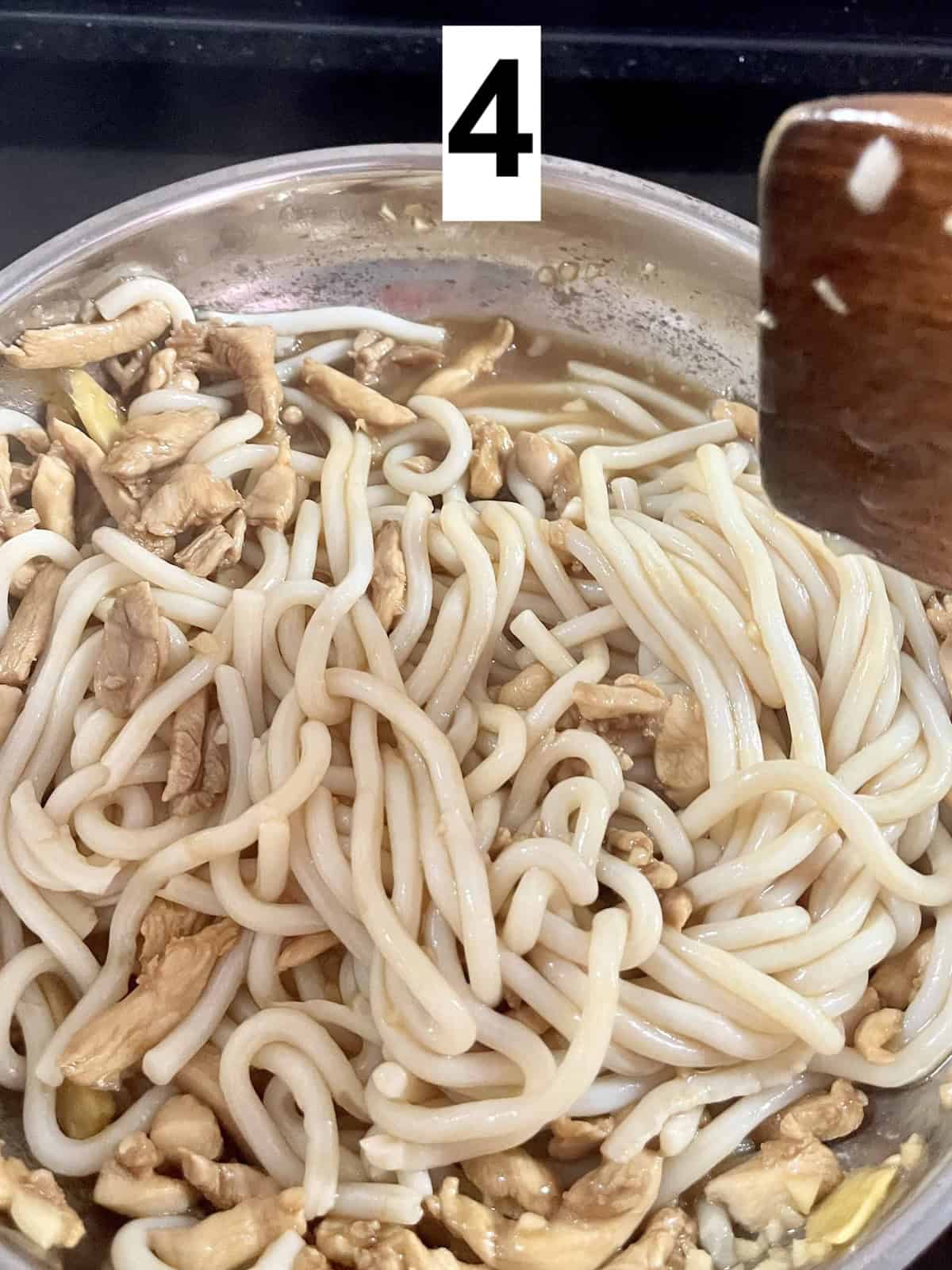 Mixing udon noodles in teriyaki sauce in a silver pan.
