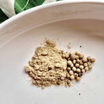 White peppercorns next to ground white pepper on a white plate.
