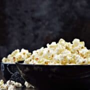 Side view of a black bowl full of popcorn.