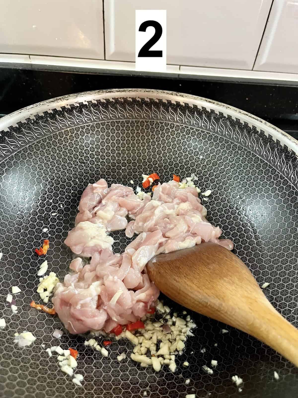 Breaking up chicken cubes in a wok.