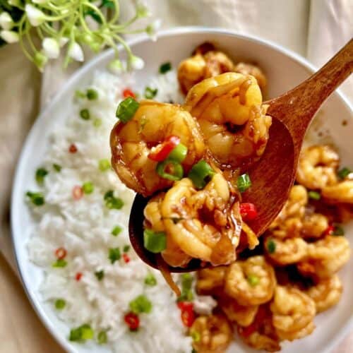 A wooden spoon picking up some Japanese teriyaki shrimp stir fry.