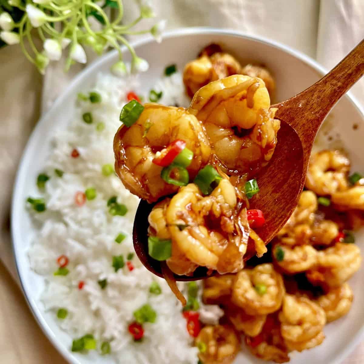 A wooden spoon picking up some Japanese teriyaki shrimp stir fry.