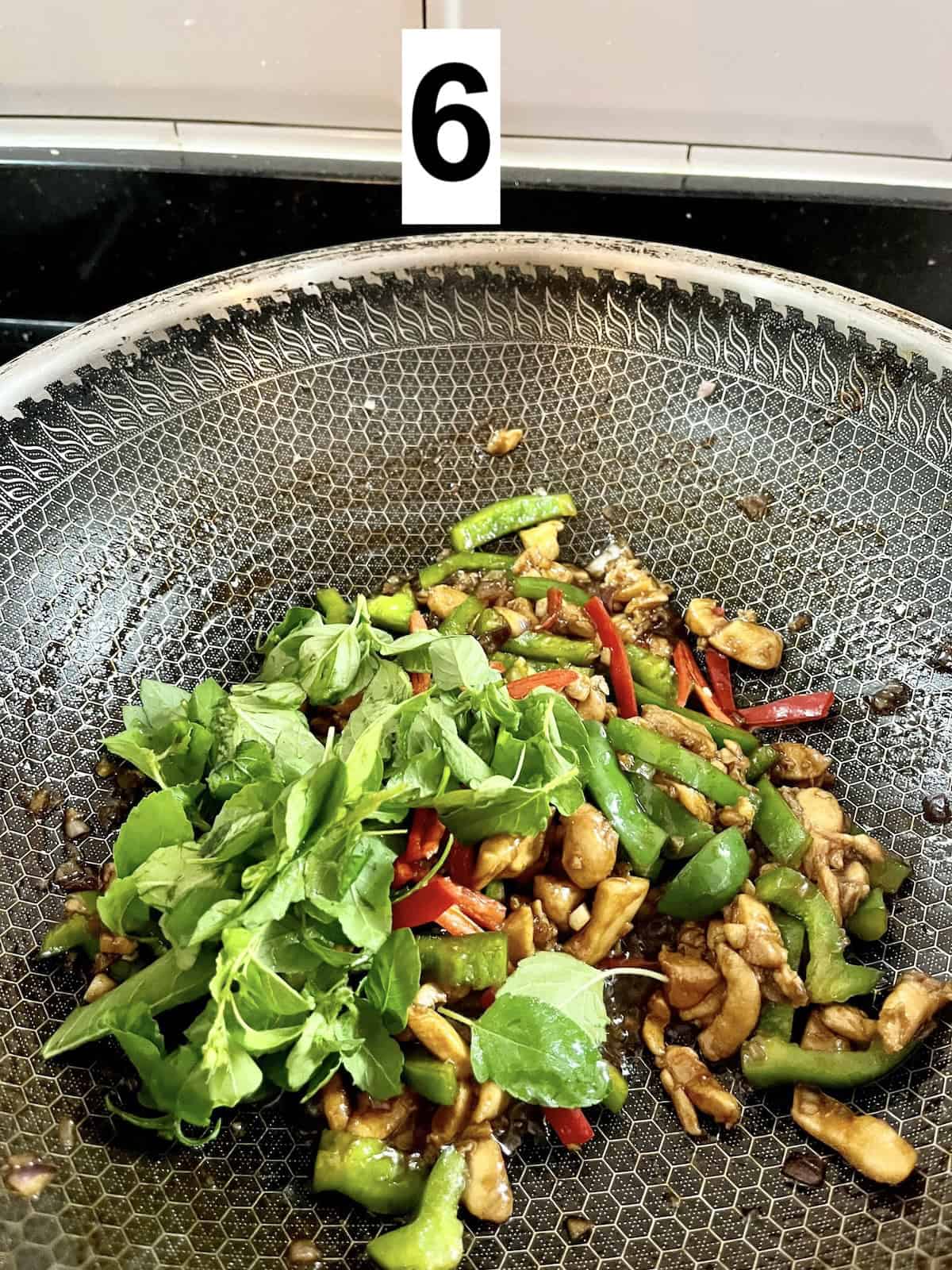 Adding Thai Basil leaves to a wok of chicken.