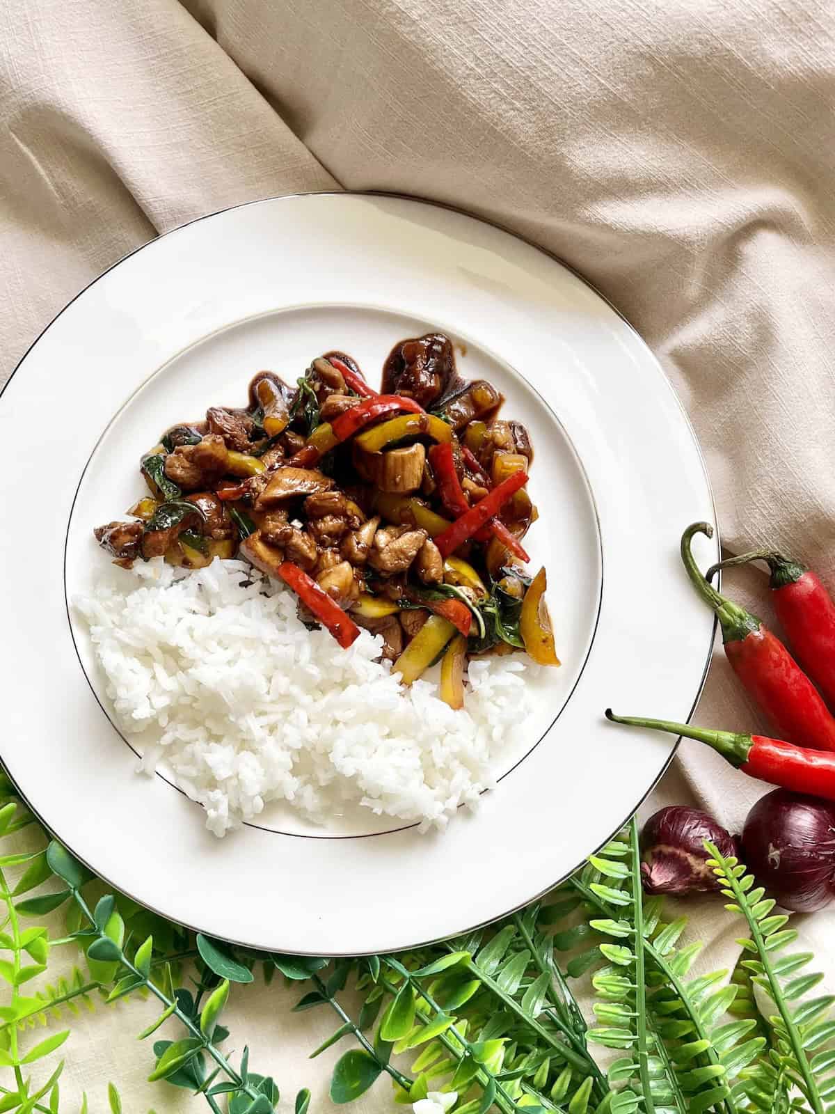 White rice and Thai-inspired chicken with Thai basil on a white plate.