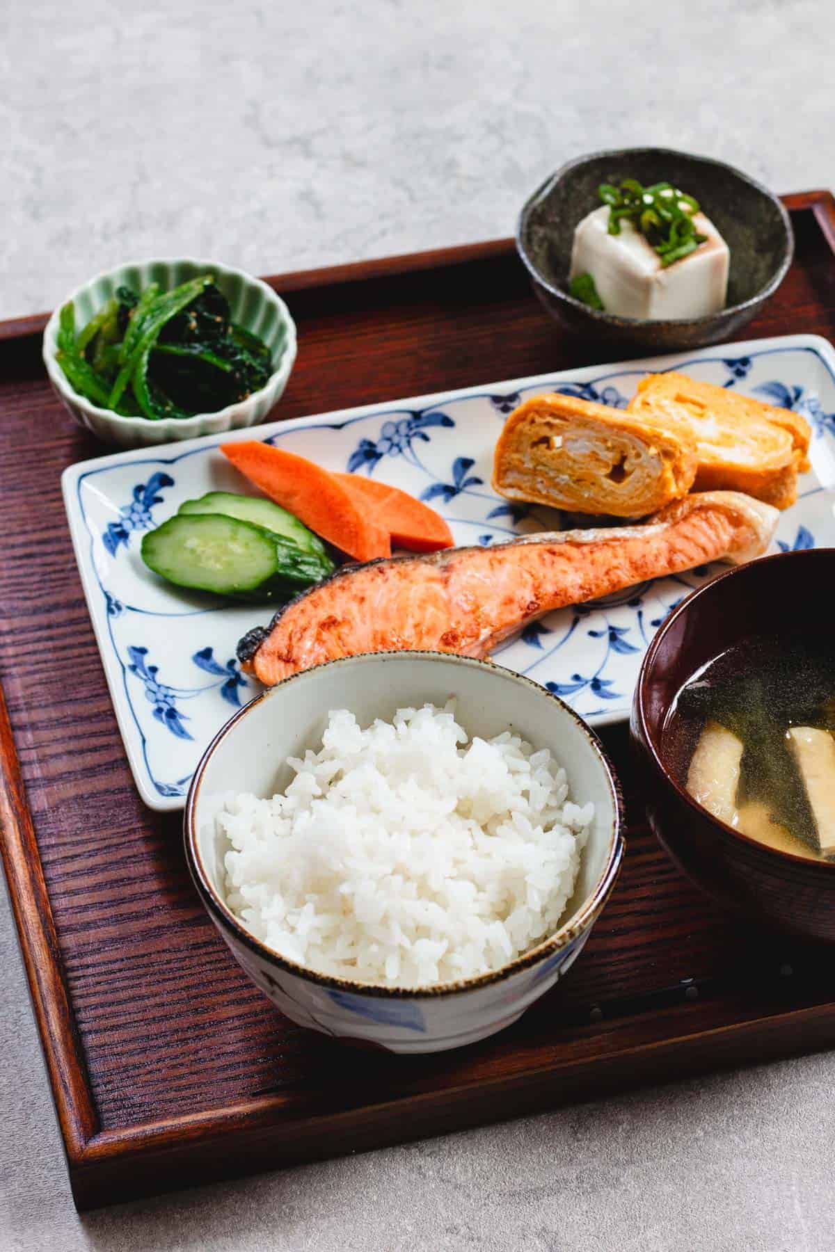 A traditional japanese breakfast of rice, pickles, and fish on a tray.