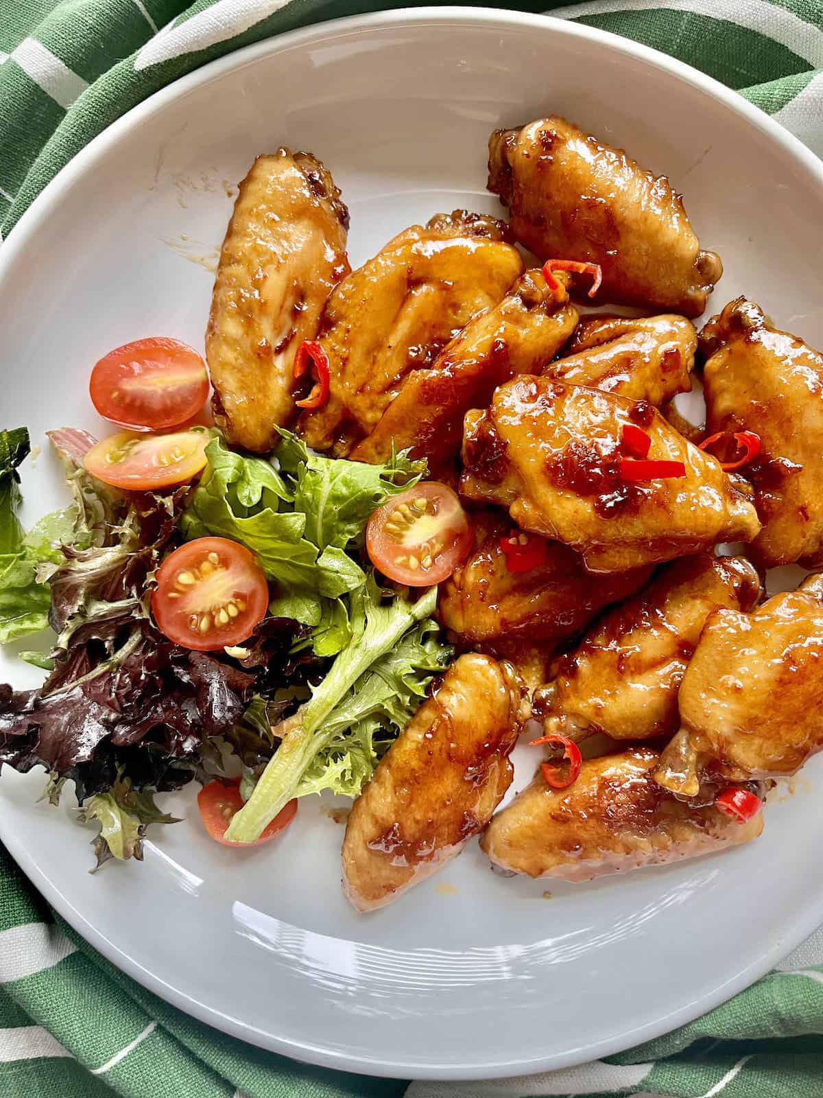 Teriyaki wings, tomatoes, and salad leaves on a white plate.
