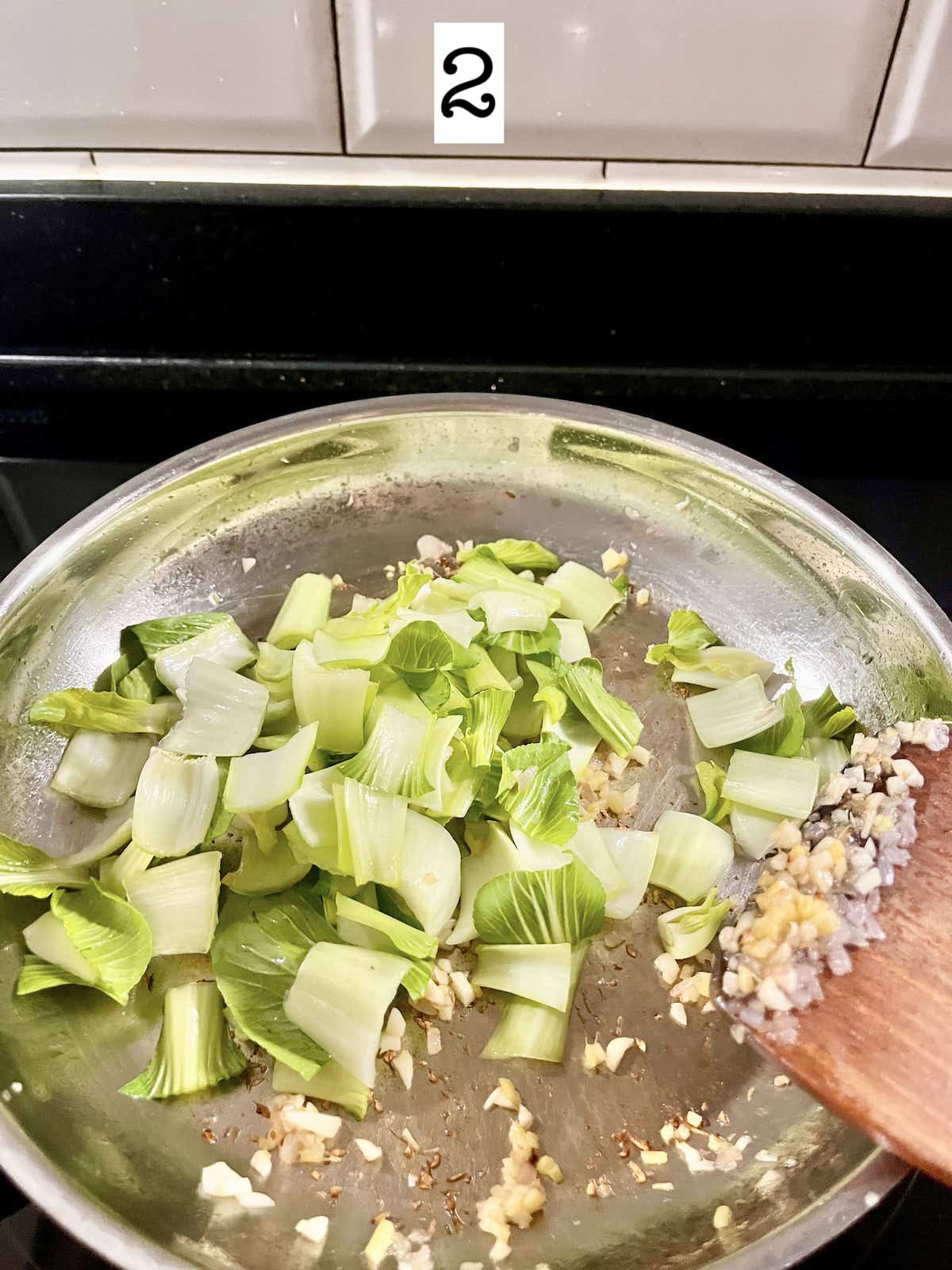 Stir-frying bok choy stems in a silver pan.