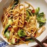 A fork twirling up some linguini chow mein noodles and green vegetables.