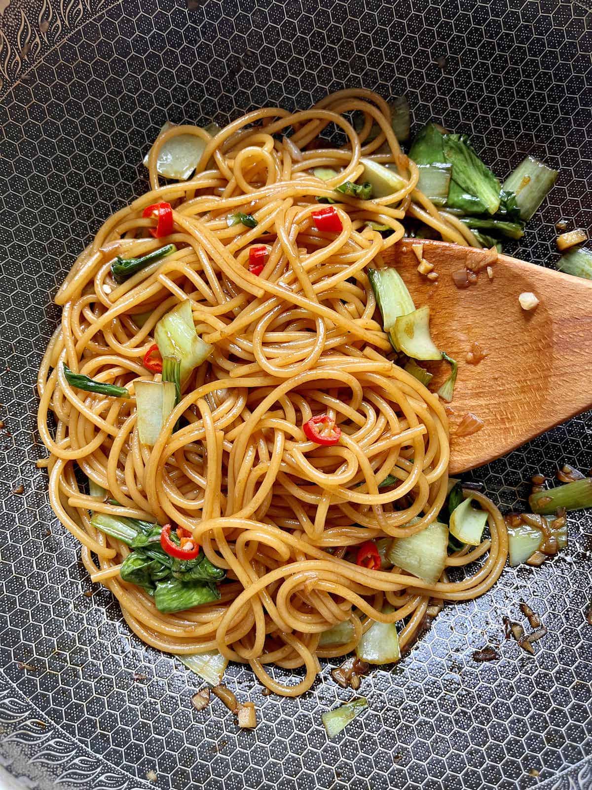 Stir frying Spaghetti Lo Mein with vegetables in a skillet.