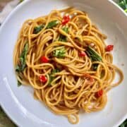 A plate of Chinese lo mein spaghetti noodles with green veggies.