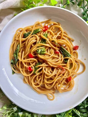 A plate of Chinese lo mein spaghetti noodles with green veggies.