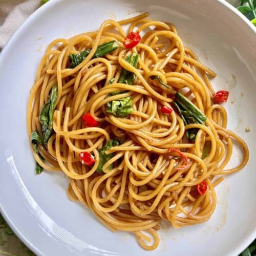 A plate of Chinese lo mein spaghetti noodles with green veggies.